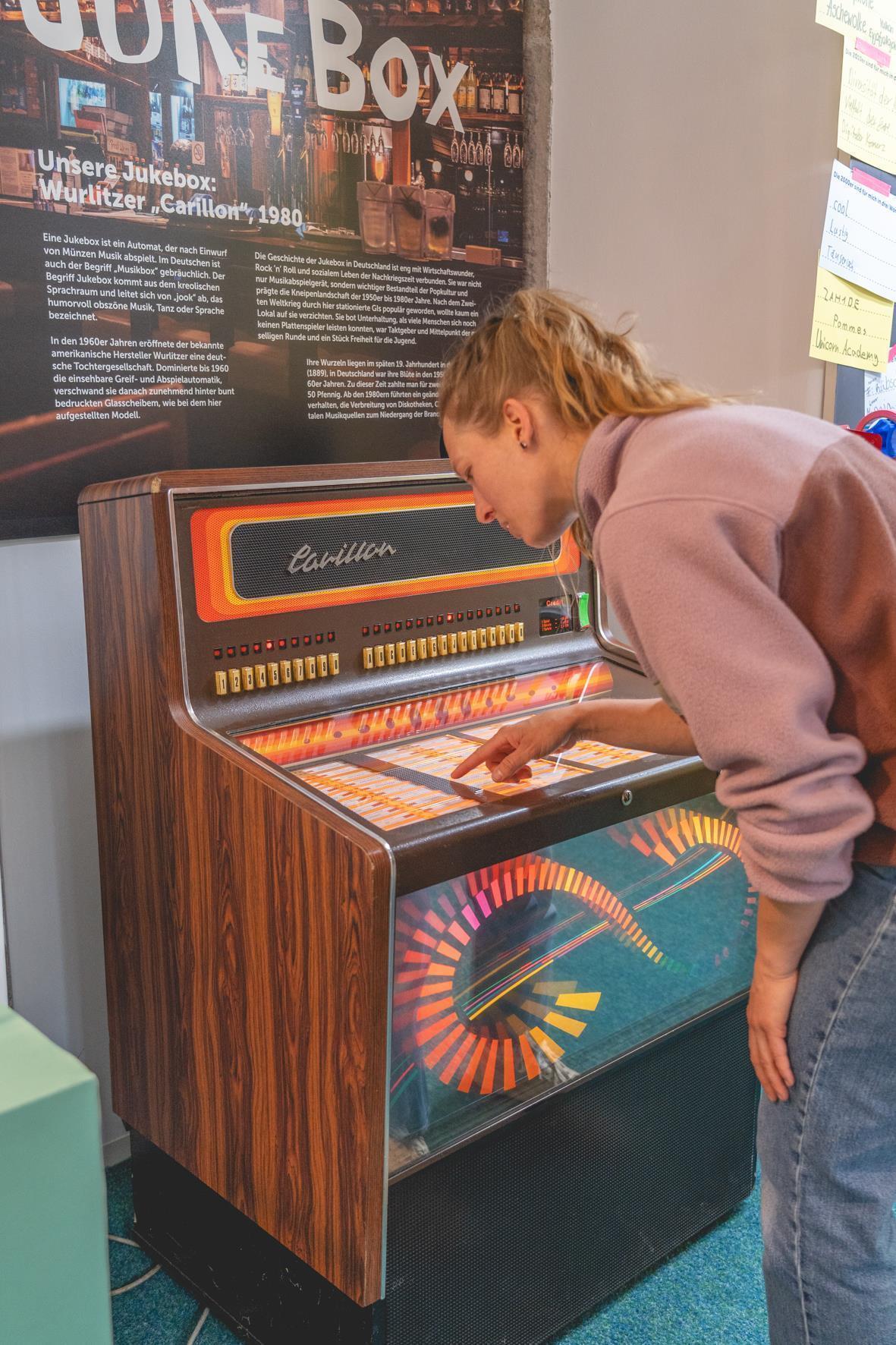 Eine Frau beugt sich über die Jukebox und sucht einen Titel