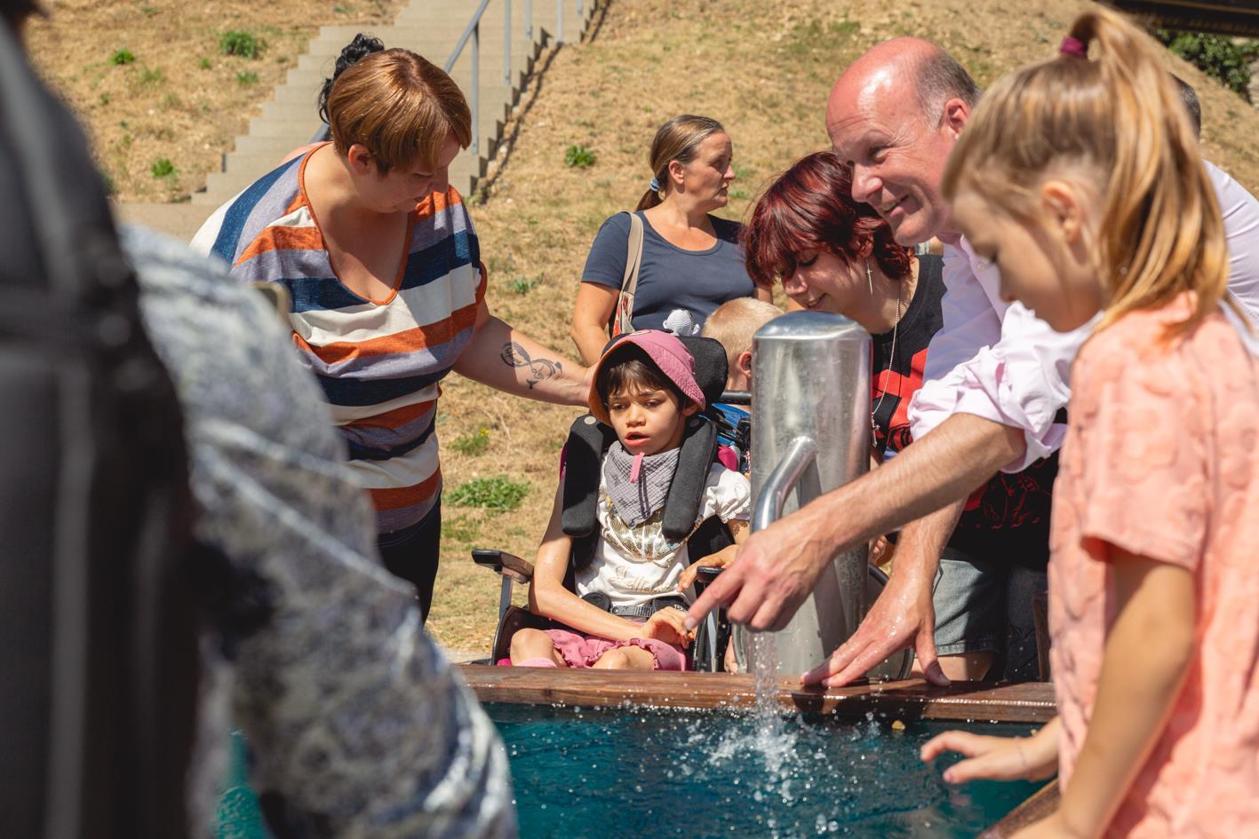 Martin Sailer mit Kindern am Brunnen während das Wasser läuft