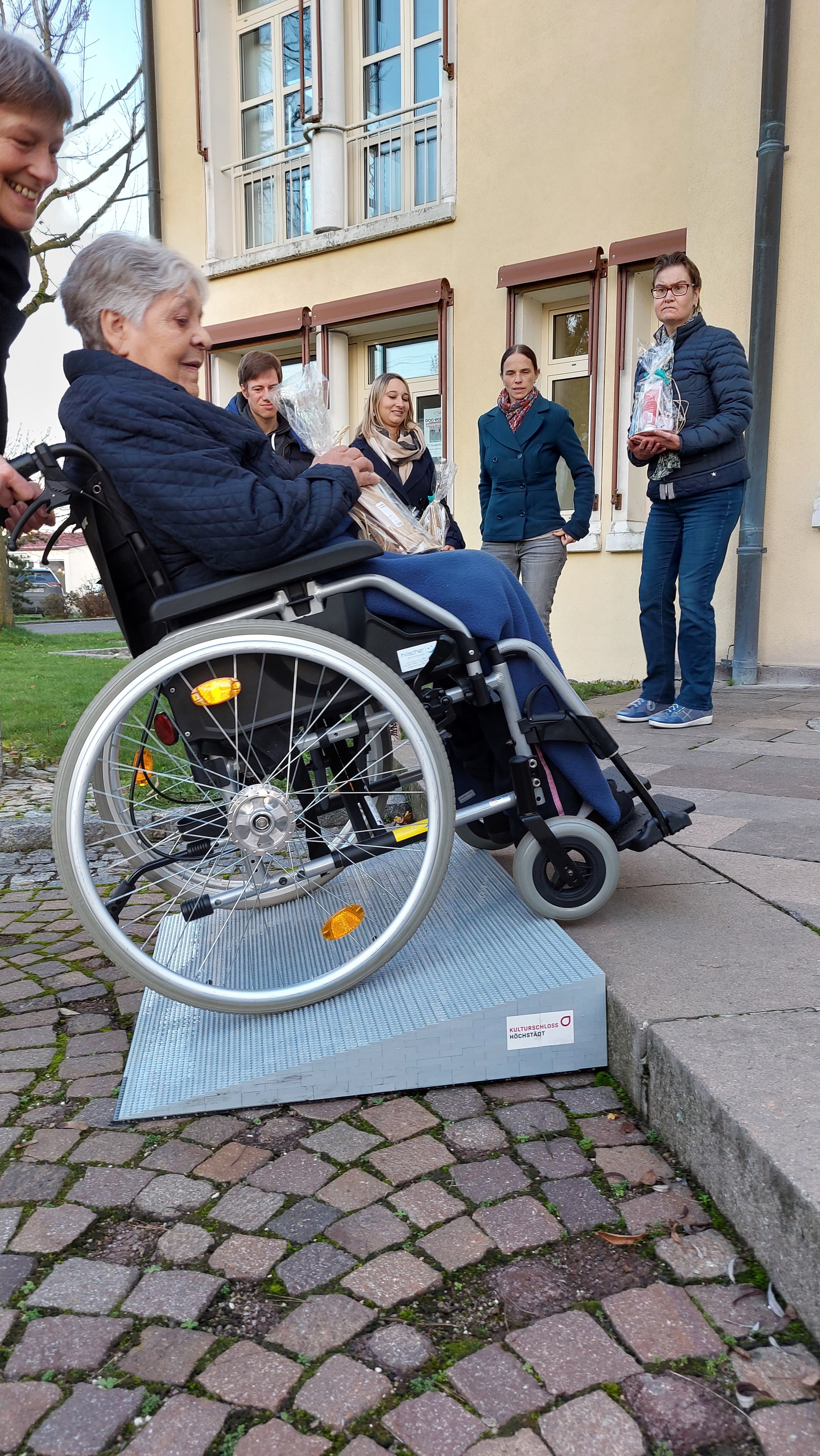Eine Person im Rollstuhl wird von einer zweiten Person die Legorampe hinauf geschoben, Nahaufnahme